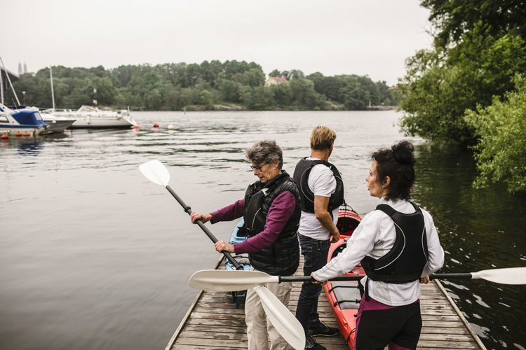 Senior women and man with kayaks and paddles on jetty during kayaking course