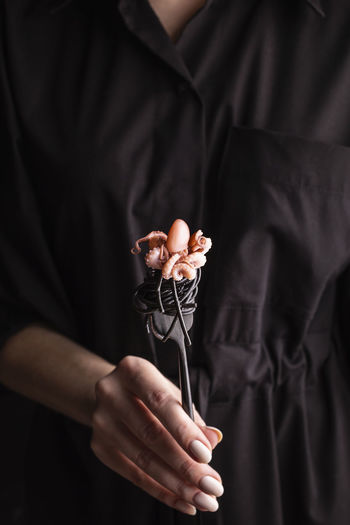 Woman holding a plate with black spaghetti with boiled octopus