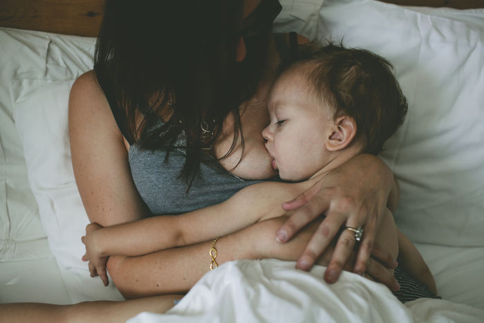 High angle view of mother breastfeeding boy while lying on bed at home
