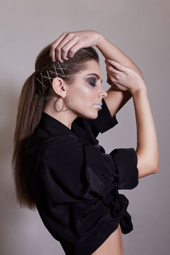Side view of sensuous young woman with eyes closed standing against gray background