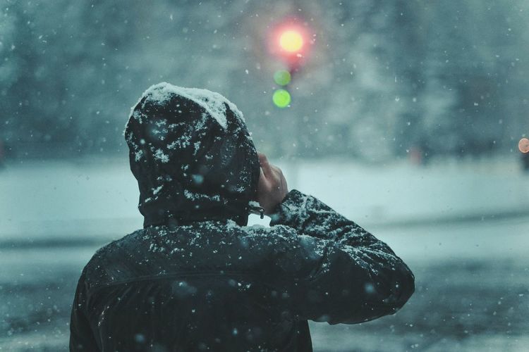 Rear view of person standing against illuminated stoplight during snowfall