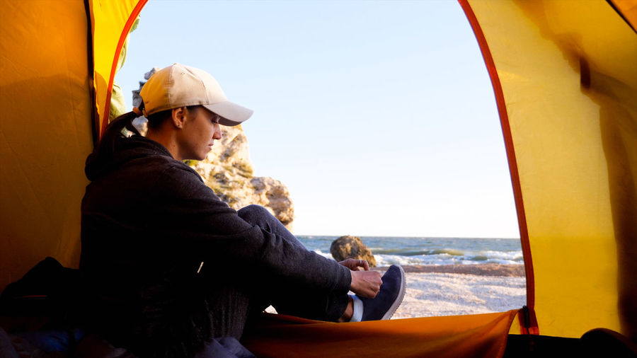 Side view of woman sitting in tent at beach