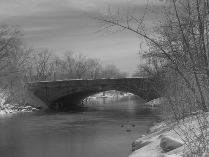 Arch bridge over river against sky during winter