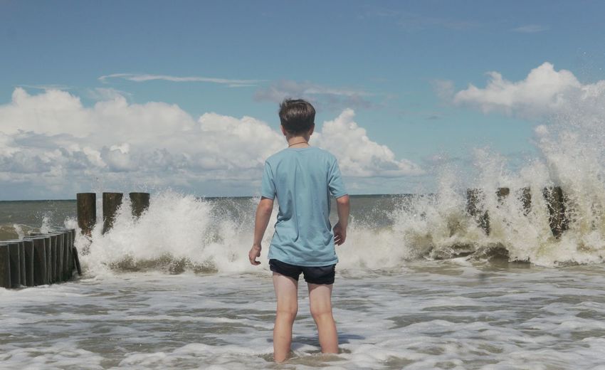 Rear view of man standing at beach against sky