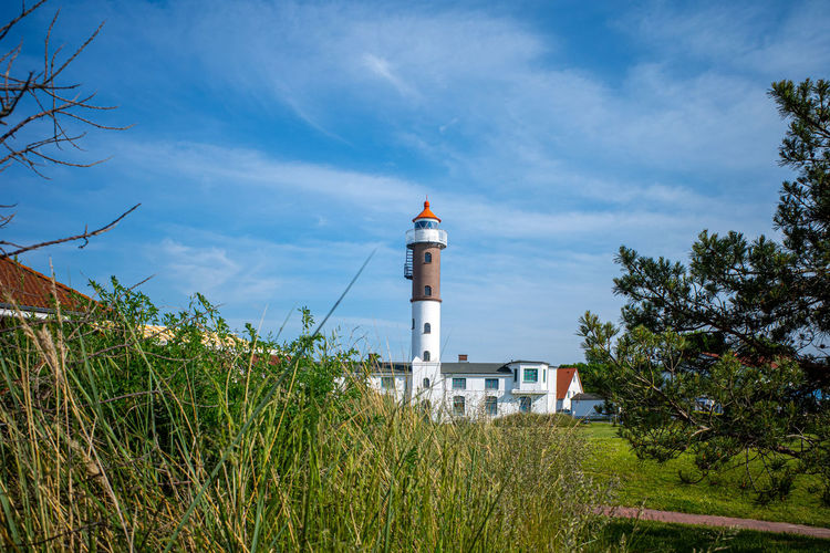 Lighthouse amidst plants and buildings against sky