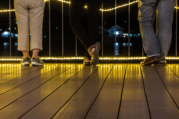 Low section of people standing on illuminated footbridge at night