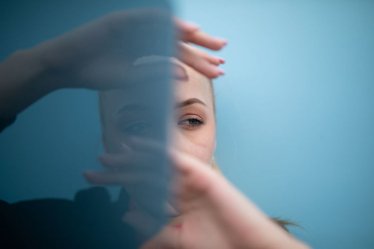 Portrait of young woman holding hands against blue background