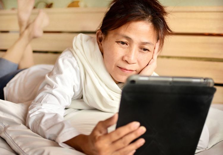 Smiling woman holding digital tablet while lying on bed at home