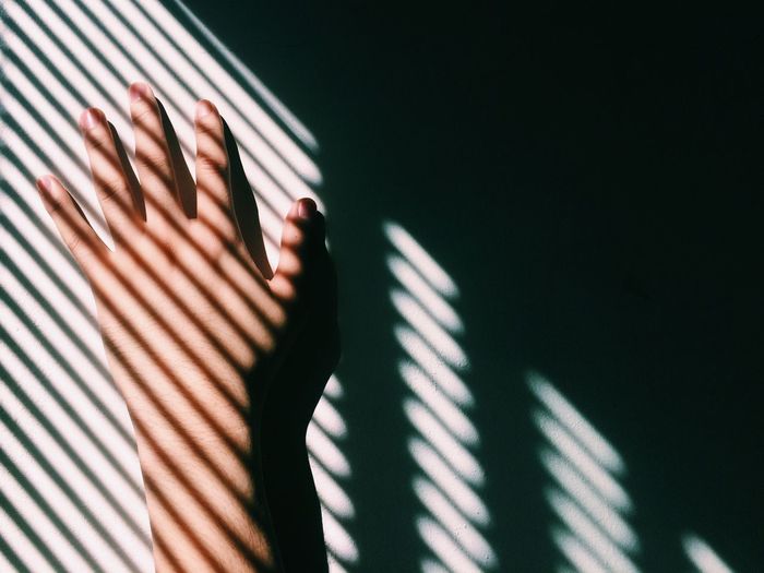Cropped image of woman hand on wall in shadow pattern