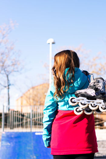 Rear view of woman carrying inline skates outdoors