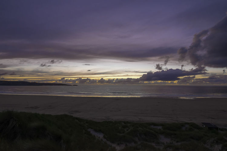 Scenic view of beach against cloudy sky during sunset