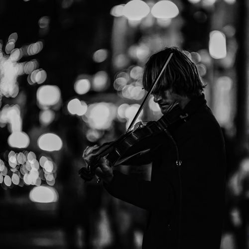 Side view of street musician playing violin at night