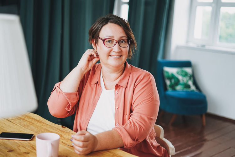 Adult charming brunette woman in glasses plus size body positive with cup of tea at home