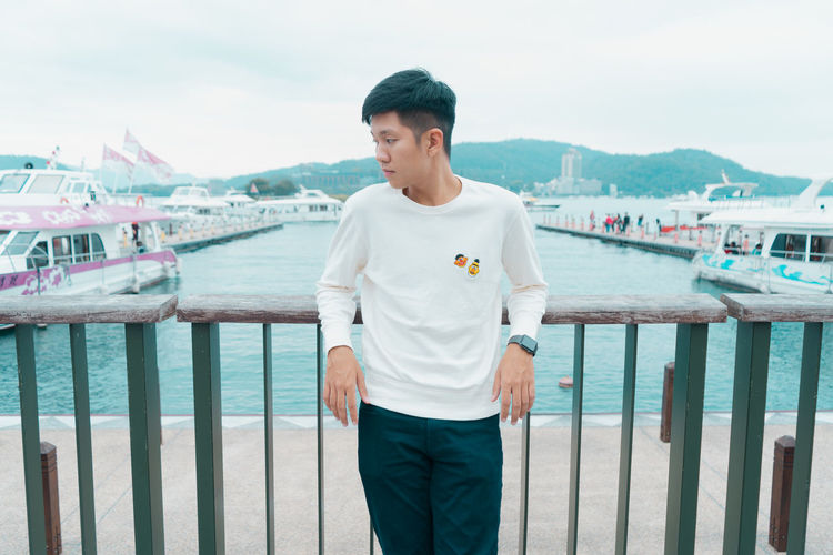 Young man standing on railing against sea