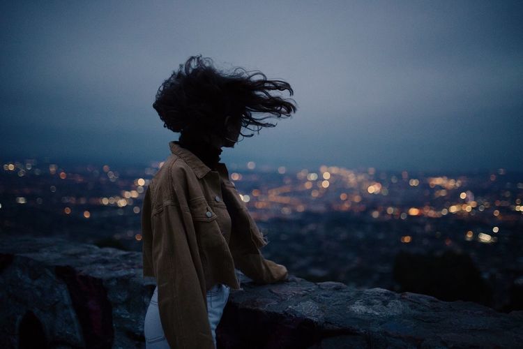 Side view of woman standing by retaining wall against sky at dusk