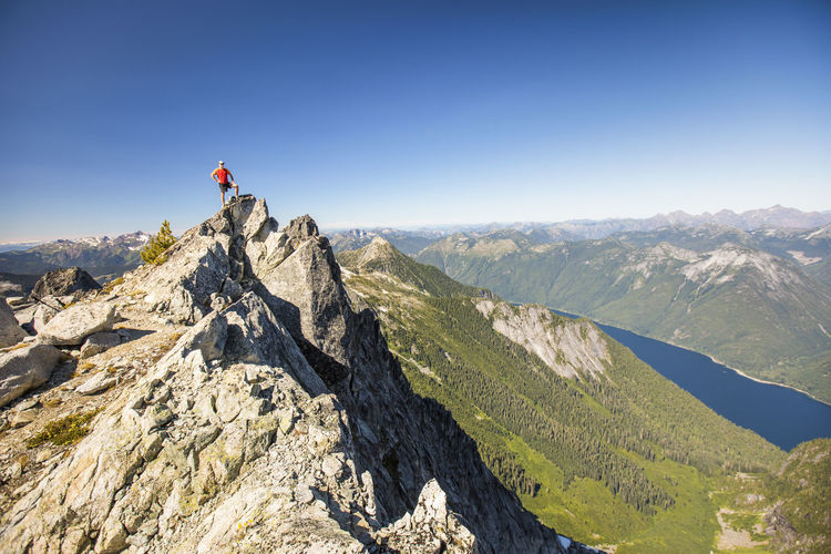 Hiker standing on mountain summit with view of lake and forest below.