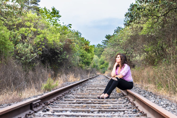 Woman sitting on railroad tracks against trees