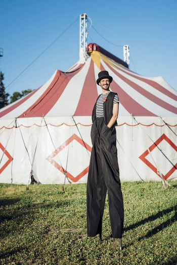 Smiling male artist standing with stilts on meadow