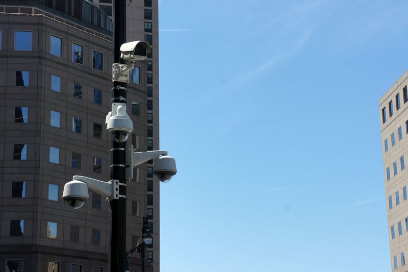 Low angle view of buildings and security cameras against sky
