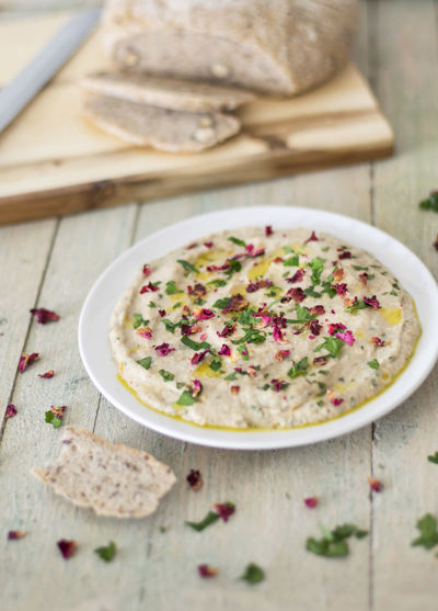 Top view of hummus on wooden table by bread loaf on chopping board