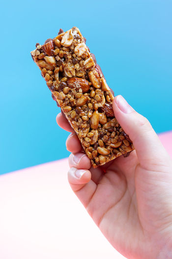 Female hand holding a protein bar on a blue and pink background.