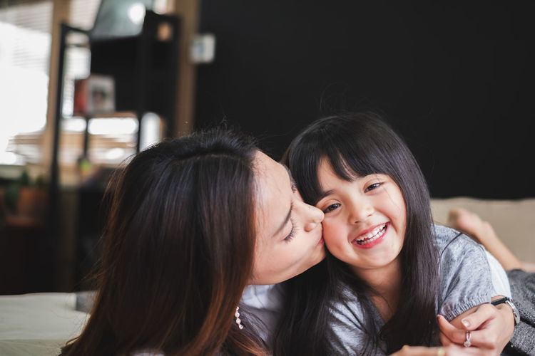 Mother kissing on cheek of cute daughter at home