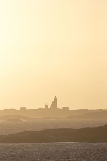 Silhouette lighthouse at seaside against sky