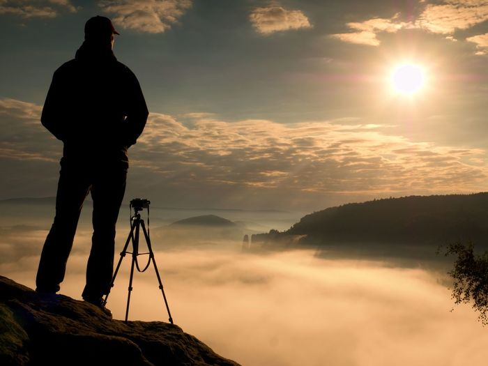 Photographer on cliff. nature photographer takes photos with mirror camera on peak of rock