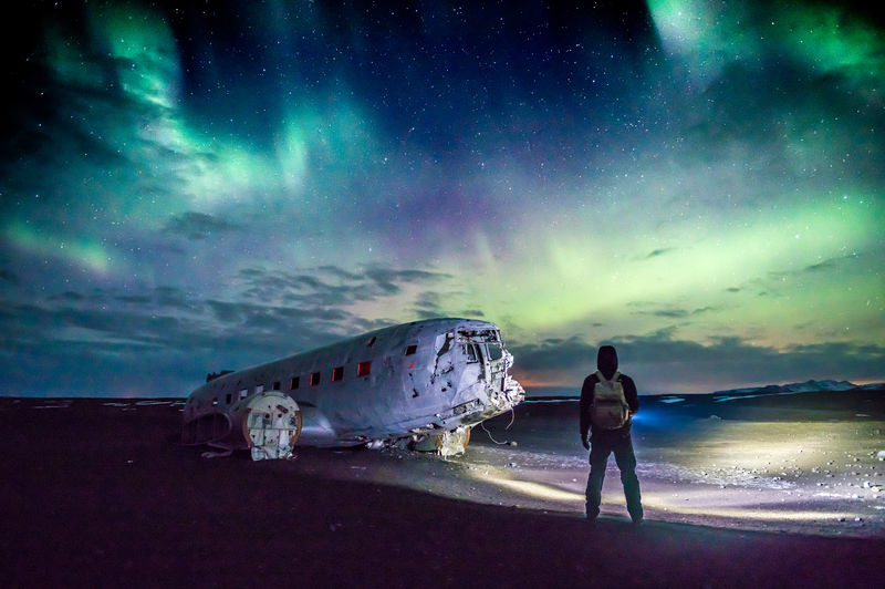 Rear view of man looking at abandoned ship in sea against sky during night