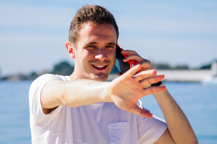 Young man on the beach using mobile phone and making denial sign with his hand
