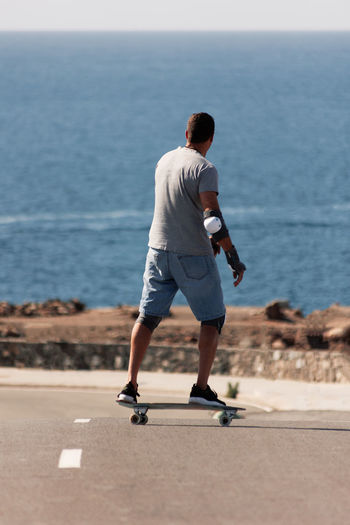A man playing figure skating on a rural road in the sun on a bright day, play surf skate near coast