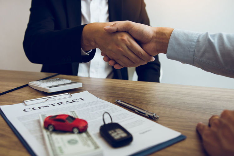 Cropped image of customer shaking hands with car salesperson sitting at desk