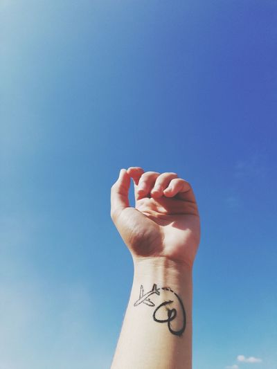 Cropped hand with tattoo against blue sky