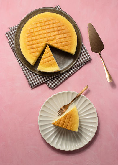 Top view of delicious cotton cheesecake served on plates near napkin and spatula on pink background