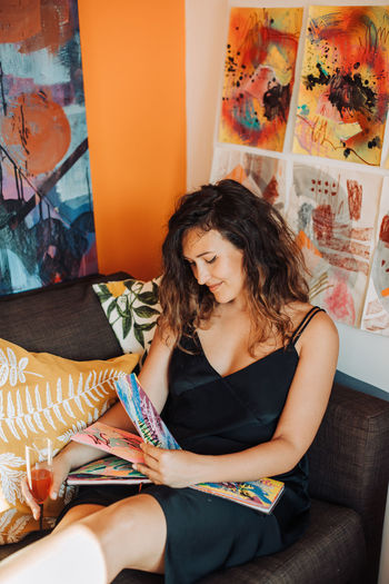 Female painter sitting on sofa in studio looking at her art album