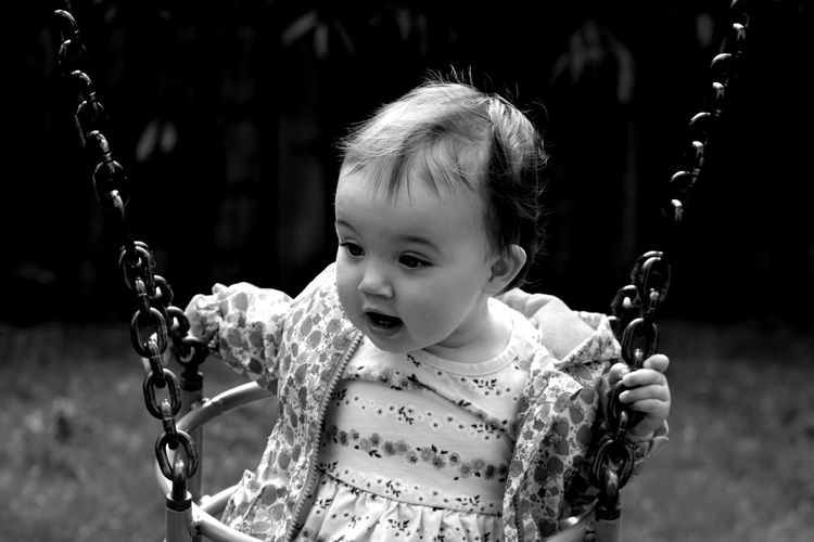 Cute baby girl sitting on swing in playground