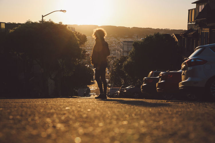 Curly hair girl on road in city against sky during sunset