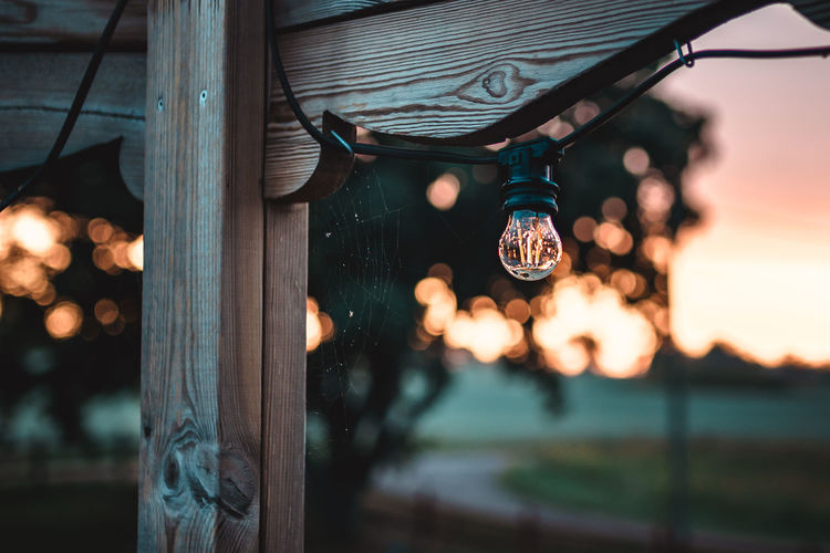 Close-up of illuminated light bulb hanging on wood