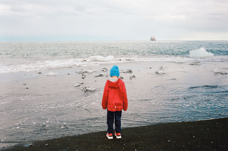 Young boy looking out at icebergs at a beach in iceland