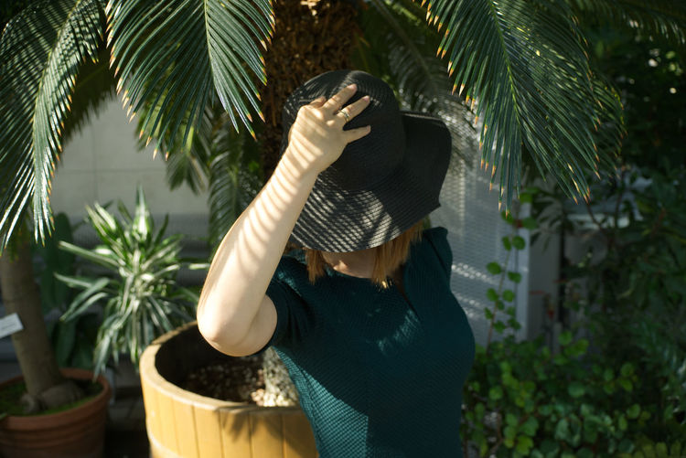 Woman wearing hat standing against tree