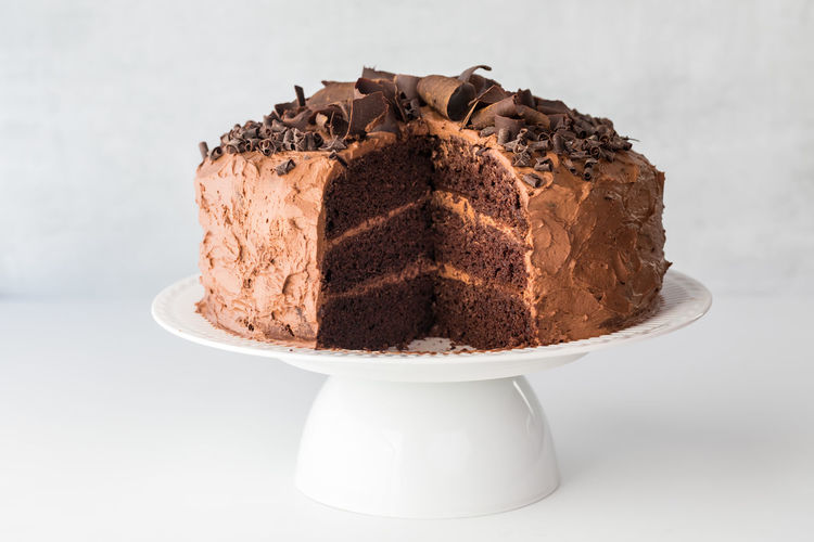 Front view of a triple layered chocolate cake with a large slice removed.