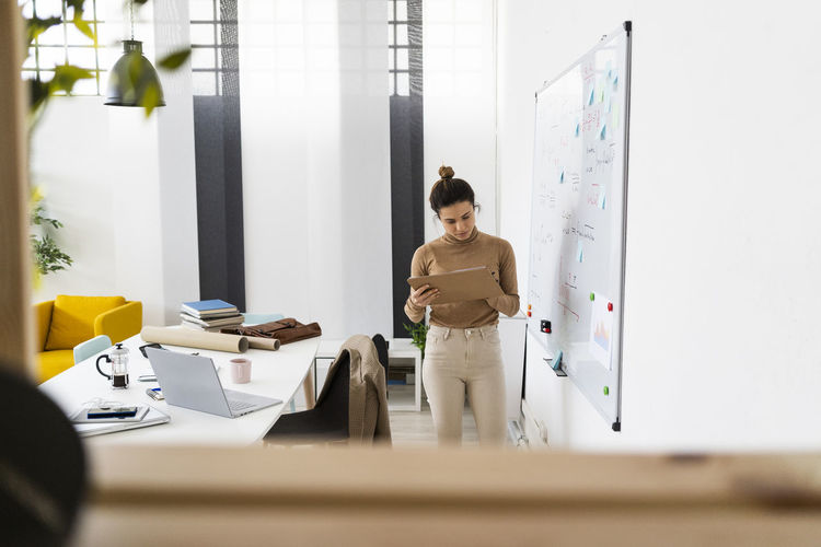 Young female student writing while standing by whiteboard