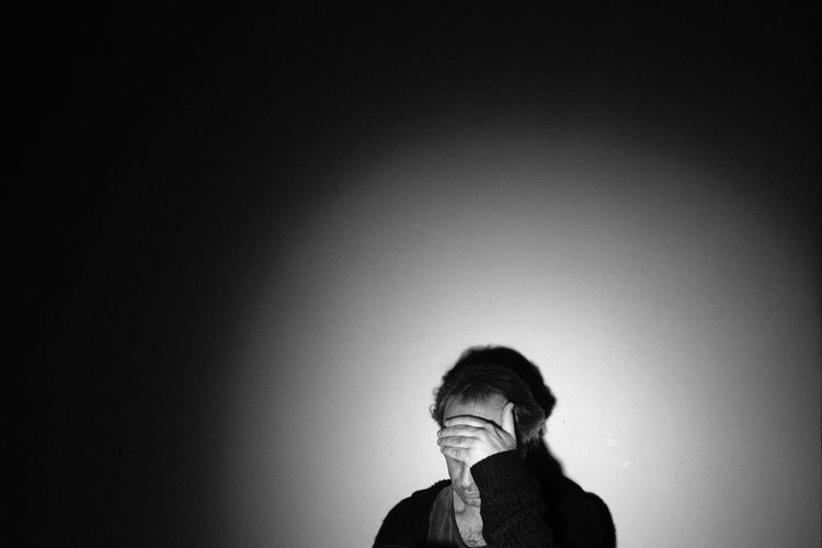 Dark portrait of young man standing against wall