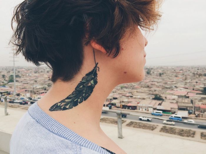 Woman with tattoo on neck against cityscape and sky