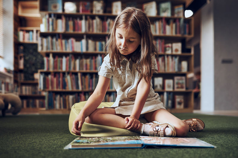 Child solving riddle in book in school library. primary school girl is involved in book with riddles