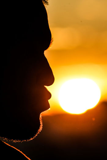 Close-up portrait of silhouette woman against illuminated orange sky