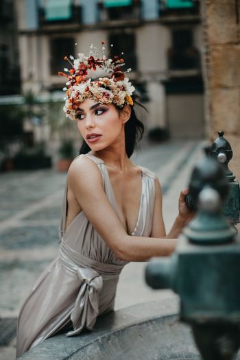 Retrato de preciosa mujer con corona de flores junto a una fuente
