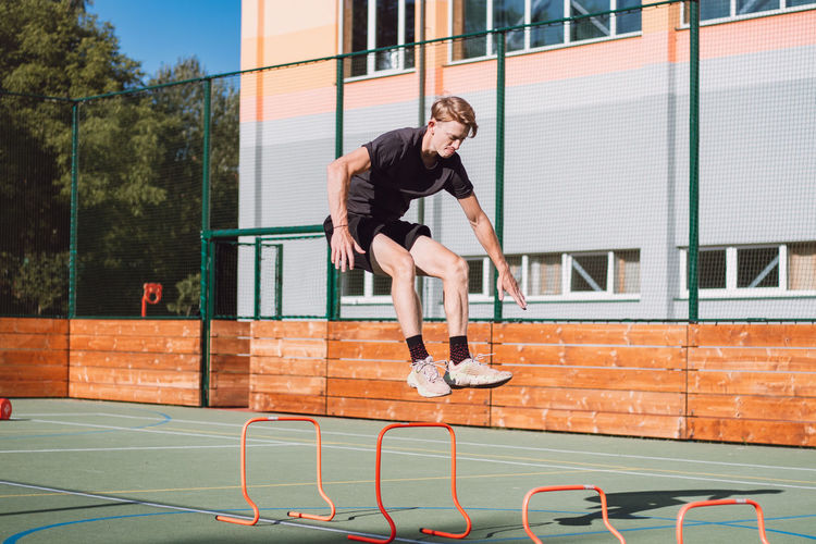 Blond boy in sportswear jumps over red obstacles to improve lower body dynamics