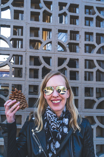 Attractive blonde haired woman holds up large pinecone to her head against geometric lattice person