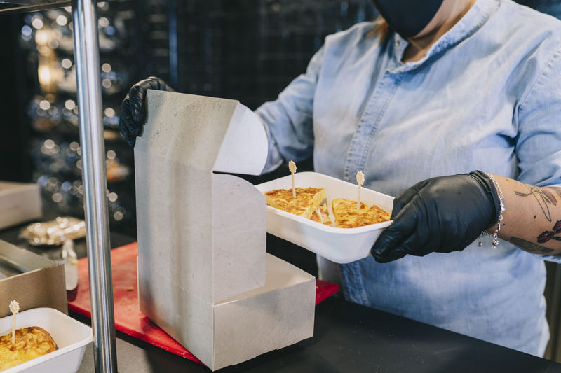 Midsection of female chef putting fresh food in cardboard box for take out at kitchen counter